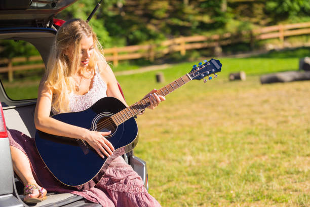 istock Hippie woman playing guitar in van car 1358296701