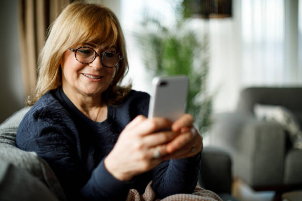 istock Smiling mature woman using mobile phone at home 1358297846