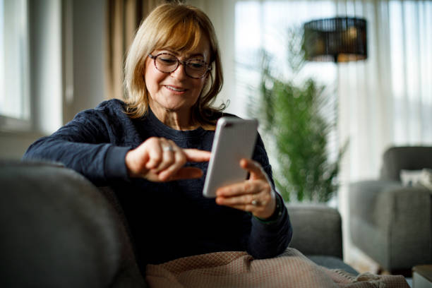 istock Smiling mature woman using mobile phone at home 1358297852
