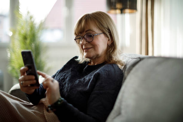 istock Smiling mature woman using mobile phone at home 1358298086
