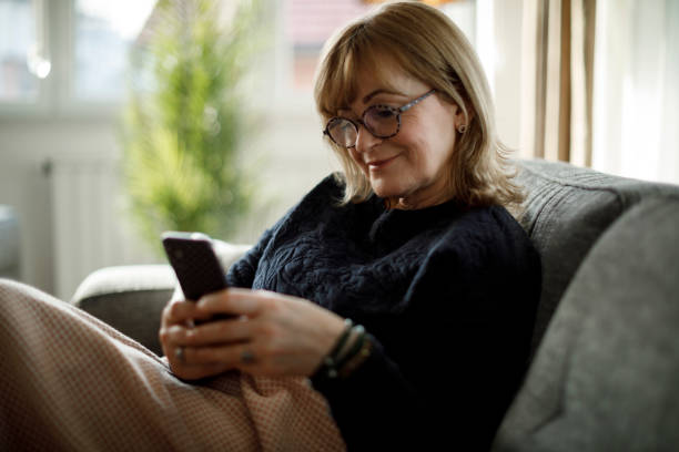 istock Smiling mature woman using mobile phone at home 1358298106