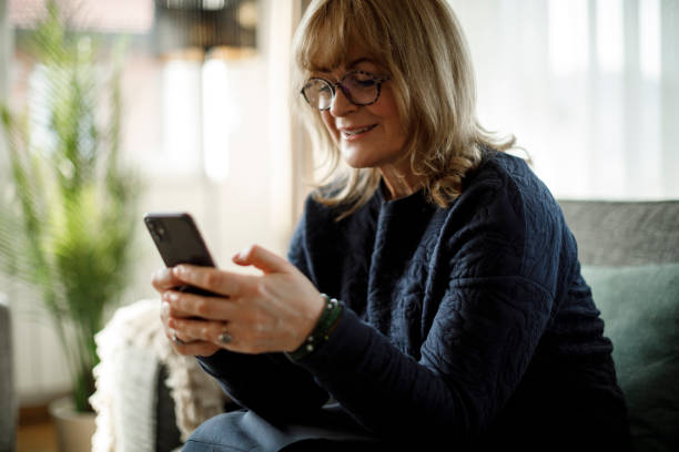 istock Smiling mature woman using mobile phone at home 1358298113