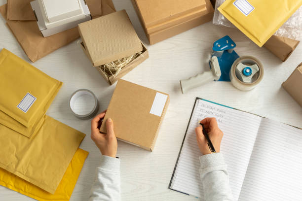 istock Warehouse worker at the workplace distributes deliveries in boxes and packages, writing in a diary. 1358298244
