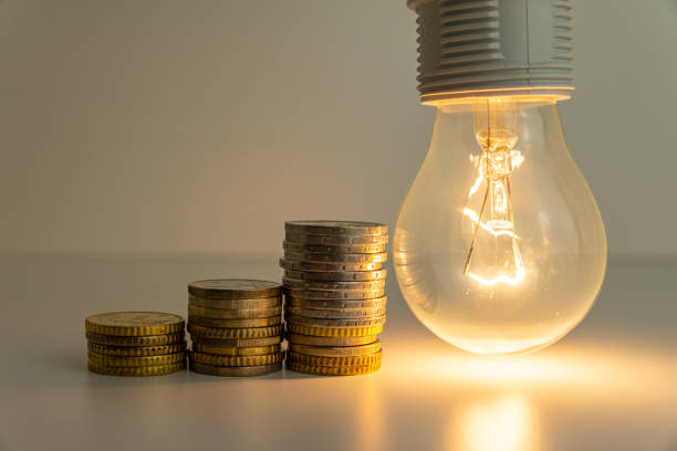Light bulb on, with coins, banknotes and energy bills next to it. stock photo