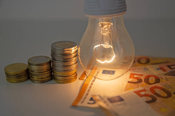 istock Light bulb on, with coins, banknotes and energy bills next to it. 1358302071