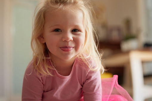 A red-haired little girl in a green T-shirt lies on a white bed at home and smiles. Portrait of a five year old girl.