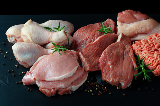Various types of fresh meat: pork, beef, turkey and chicken on a black table