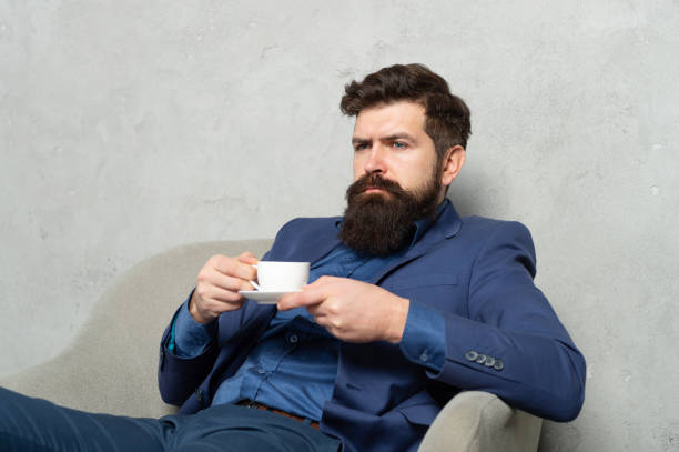 brodaty mężczyzna relaksuje się pijąc herbatę lub kawę w fotelu wypoczynkowym podczas przerwy w pracy, relaksując się - content businessman executive director manager zdjęcia i obrazy z banku zdjęć
