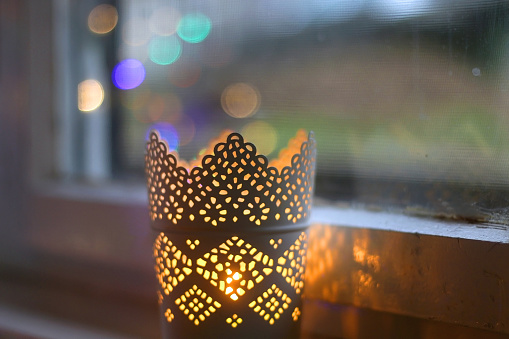 Lit candles in the window sill. Colorful bokeh lights reflected in glass. Selective focus.