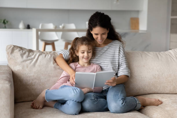 istock Smiling young mother reading book to small daughter. 1358310816