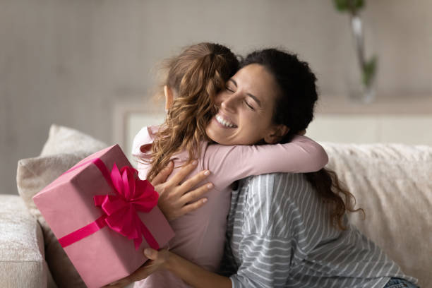 Emotional happy young mother feeling thankful getting gift from kid. Emotional happy young mother feeling thankful getting surprise gift, cuddling little preschool kid daughter, celebrating birthday or special event together at home, joyful family sincere relations. birthday wishes for daughter stock pictures, royalty-free photos & images