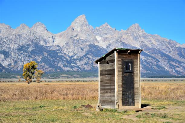 The Grand Tetons and Outhouse The Grand Teton Mountains rise above the valley and an outhouse in the Mormon Row Historic District during autumn in Grand Teton National Park. snake river valley grand teton national park stock pictures, royalty-free photos & images