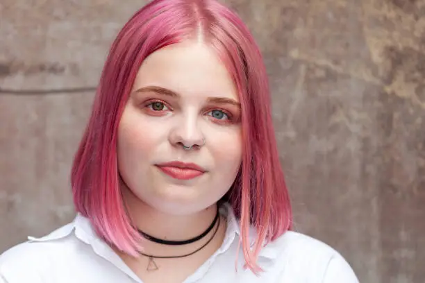 Close up outdoors portrait of attractive 20 year old woman with pink hair in white shirt
