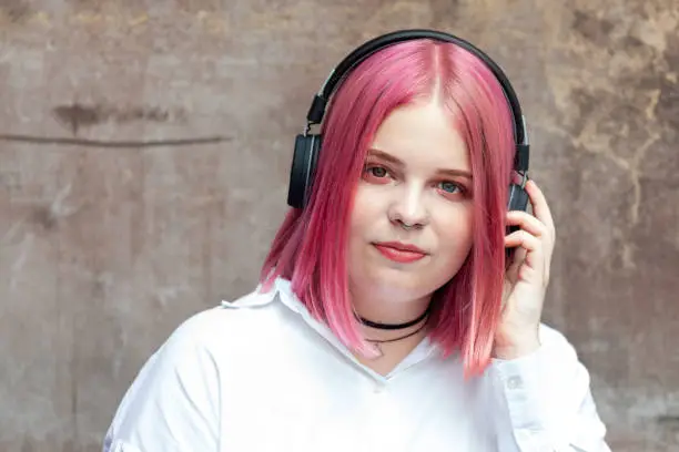 Close up outdoors portrait of attractive 20 year old woman with pink hair in white shirt with headphones