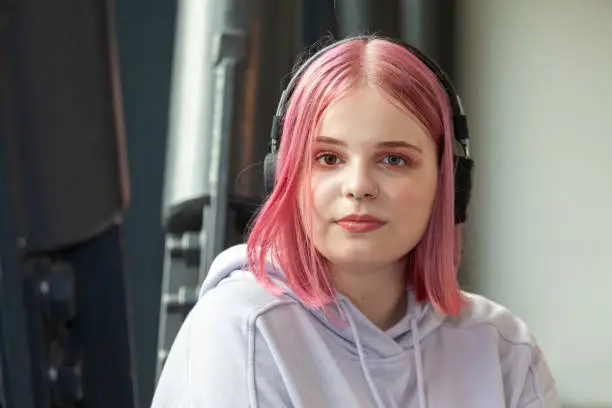 Close-up outdoors portrait of attractive 20 year old woman with pink hair in purple hooded shirt with headphones