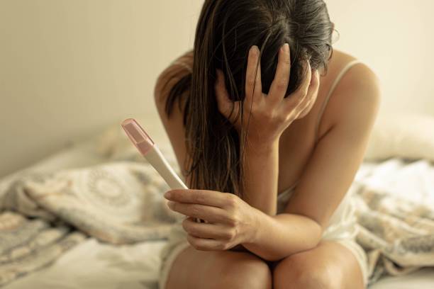 Frustrated worried woman holding a pregnancy test, waiting for the results. Infertility problems. A woman with her head down sitting on her bed holding a pregnancy test unsure and saddened. awful taste stock pictures, royalty-free photos & images