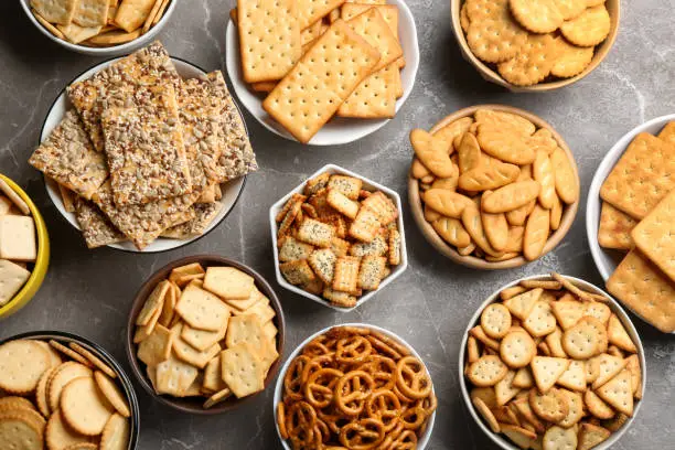 Different delicious crackers in bowls on grey table, flat lay
