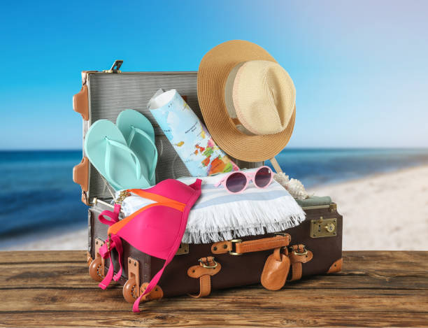 istock Open vintage suitcase packed for summer vacation on wooden surface against sandy beach 1358329723
