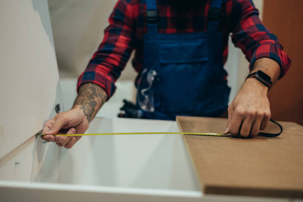istock Young male carpenter working in workshop and measuring with meter 1358331058