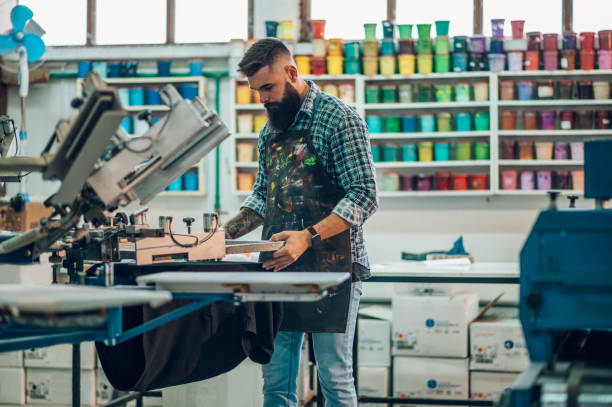 travailleur utilisant une machine à imprimer dans un atelier - fashion industry photos et images de collection