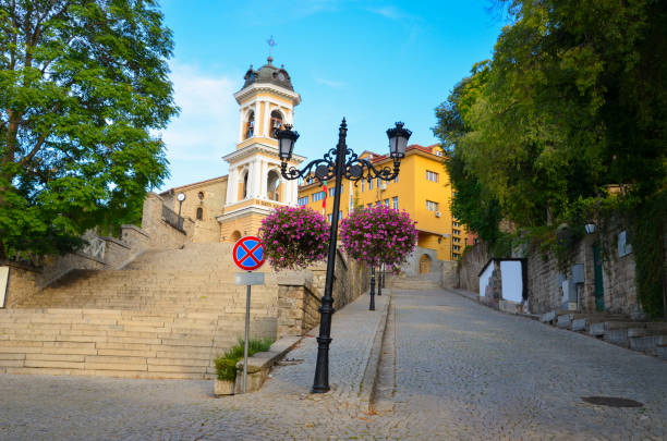 Beautiful old town with the Holy Mother of God Church in Plovdiv, Bulgaria. Purple blooming flowers, cobbled street and traditional houses. Blue sky above.