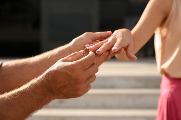 istock Man putting engagement ring on his girlfriend's finger outdoors, closeup 1358332929