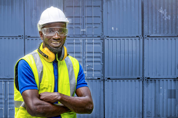 istock African workers man engineering standing with confident with blue working suite dress and safety helmet. manual worker in front container background. Concept of smart industry worker operating. 1358334865