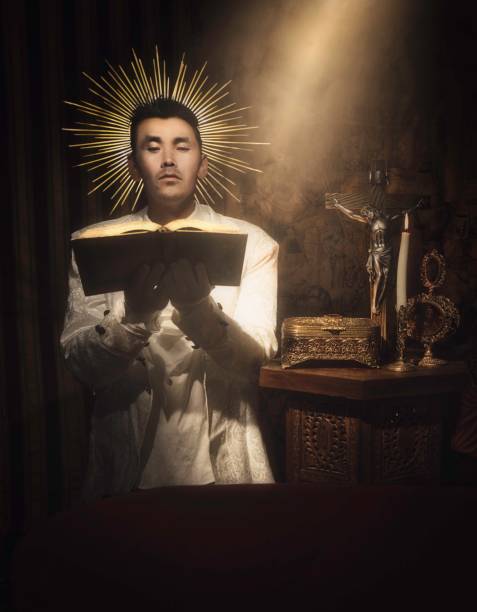 This image showcases a fantasy religious iconography scene with an angelic asian male kneeling and reading holy scripture with a halo around his head.