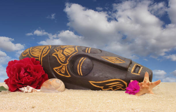 wooden tiki mask on sand with flowers and blue sky background - shell sea souvenir island imagens e fotografias de stock