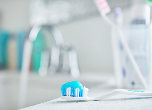 Plastic toothbrush with toothpaste in front of plastic toothbrush holder in modern bathroom