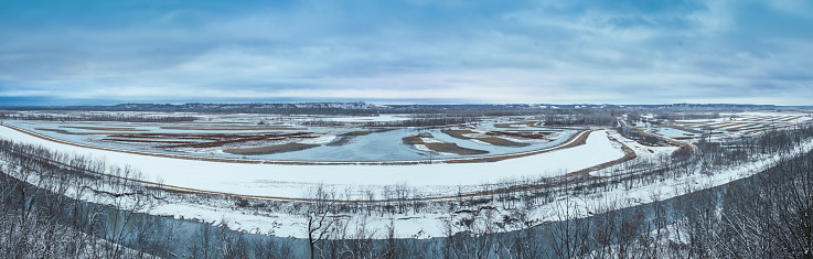 Panoramic view of Missouri River floodplain converted into conservation area in winter; fields covered with snow; water crosses the area