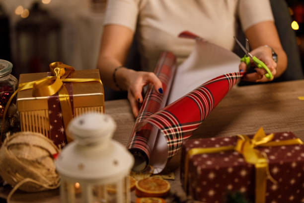 istock Young woman unrolling plaid wrapping paper to wrap a Christmas present 1358363354