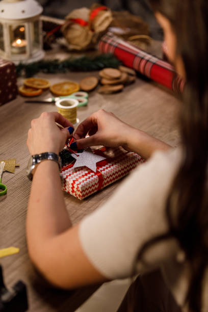 istock Woman adding a star shaped ornament as decoration on a Christmas present she is preparing 1358363449