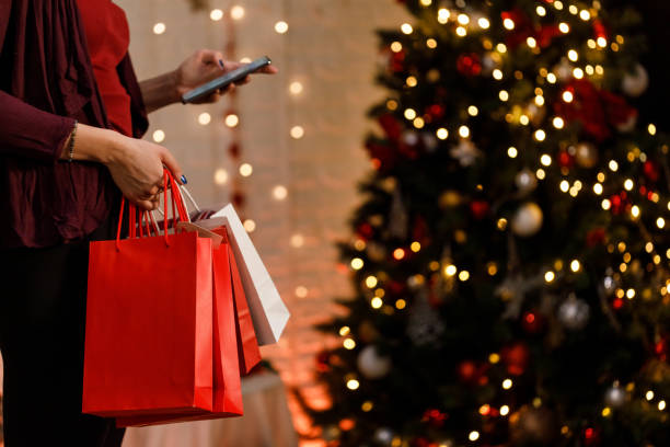 istock Woman using smart phone and holding Christmas gift bags 1358363776