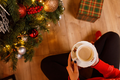 Copy space shot of unrecognizable young woman sitting on the floor and enjoying a cup of coffee after she finished decorating the Christmas tree.