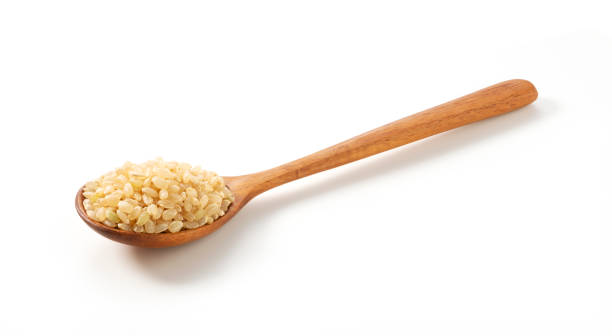 Brown rice in a wooden spoon placed on a white background. Brown rice in a wooden spoon placed on a white background.  A pile of brown rice. genmai stock pictures, royalty-free photos & images