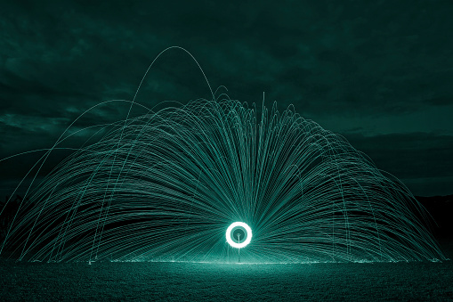 A wheel of fire created using steel wool alight on a bicycle wheel at night to provide a dark backdrop and green sparks
