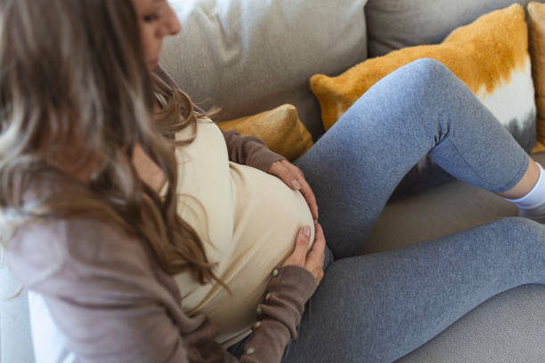 mujer adulta joven embarazada descansando en el sofá de casa, sintiéndose mal. la joven embarazada ha sufrido dolores de cabeza sentado en el sofá. síntomas del embarazo - backache pain women illness fotografías e imágenes de stock