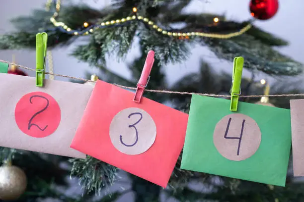 Close up Christmas Advent calendar with colorful envelopes two, three, four near Christmas tree. Homemade surprise for children.