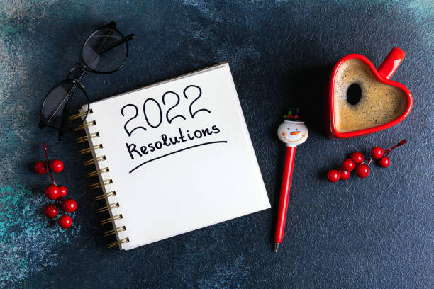 istock New year resolutions 2022 on desk. 2022 new year resolutions on blue background with coffee cup, notebook and christmas decorations. New year goals, plan, resolutions, business 1358391652