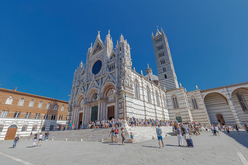 Siena, Italy - August 19, 2021: street view of Duomo di Siena, many tourists are visible waiting in line under the sun.