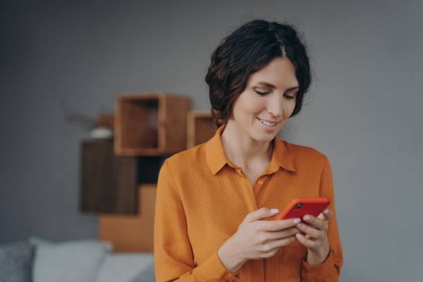 istock Young smiling hispanic lady holding smartphone, looking at screen with smile and texting sms 1358401627