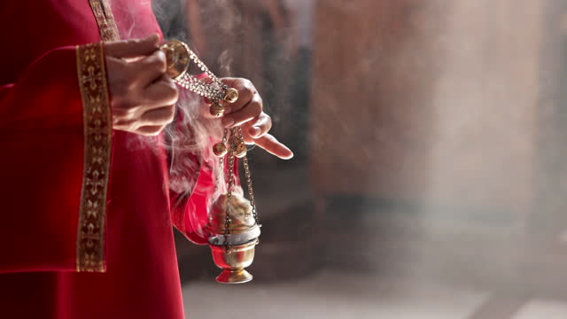 B-roll of unrecognizable priest in red gown, holding the insense burner, during religious event