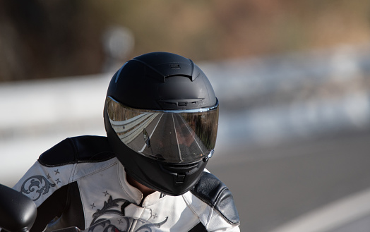 A motorcyclist with a protective helmet in his hand next to his motorcycle. Taken at night. Photograph