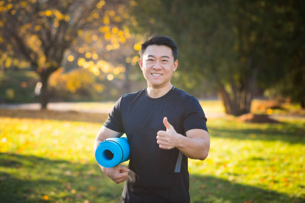 istock Active handsome male yogi walks in a park strolling forest before or after a workout. Young asian athletic man athlete goes to yoga class with a fitness mat in his hands. Outdoors Healthy lifestyle 1358404789