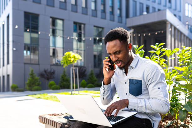 istock african american male freelancer working remotely online broker with exchanges stocks talking on mobile phone and laptop Merchant seller. Male in city park a bench modern urban background business man 1358406049