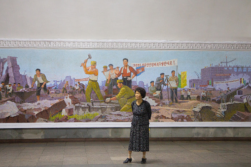 Unidentified woman standing in front of socialist realist mosaic at Pyongyang Metro in North Korea. It is built from 1965 to 1987 and it's one of the deepest metros in the world.
