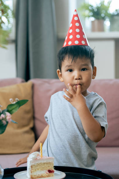 istock Adorable little boy in birthday cap tasting cake and looking at camera 1358407997