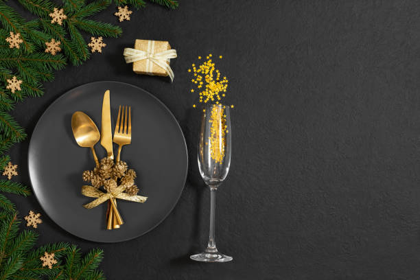 Christmas table setting with golden festive decorations on black background. New Year party. Copy space, top view, flat lay.