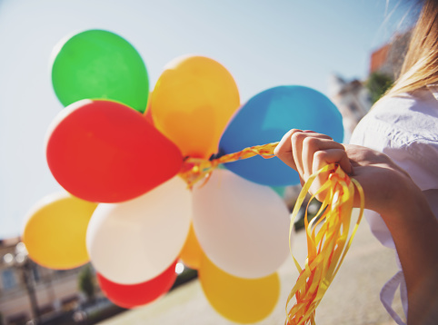 Young girl walking outdoor on summer, holding bunch of colorful helium balloons.